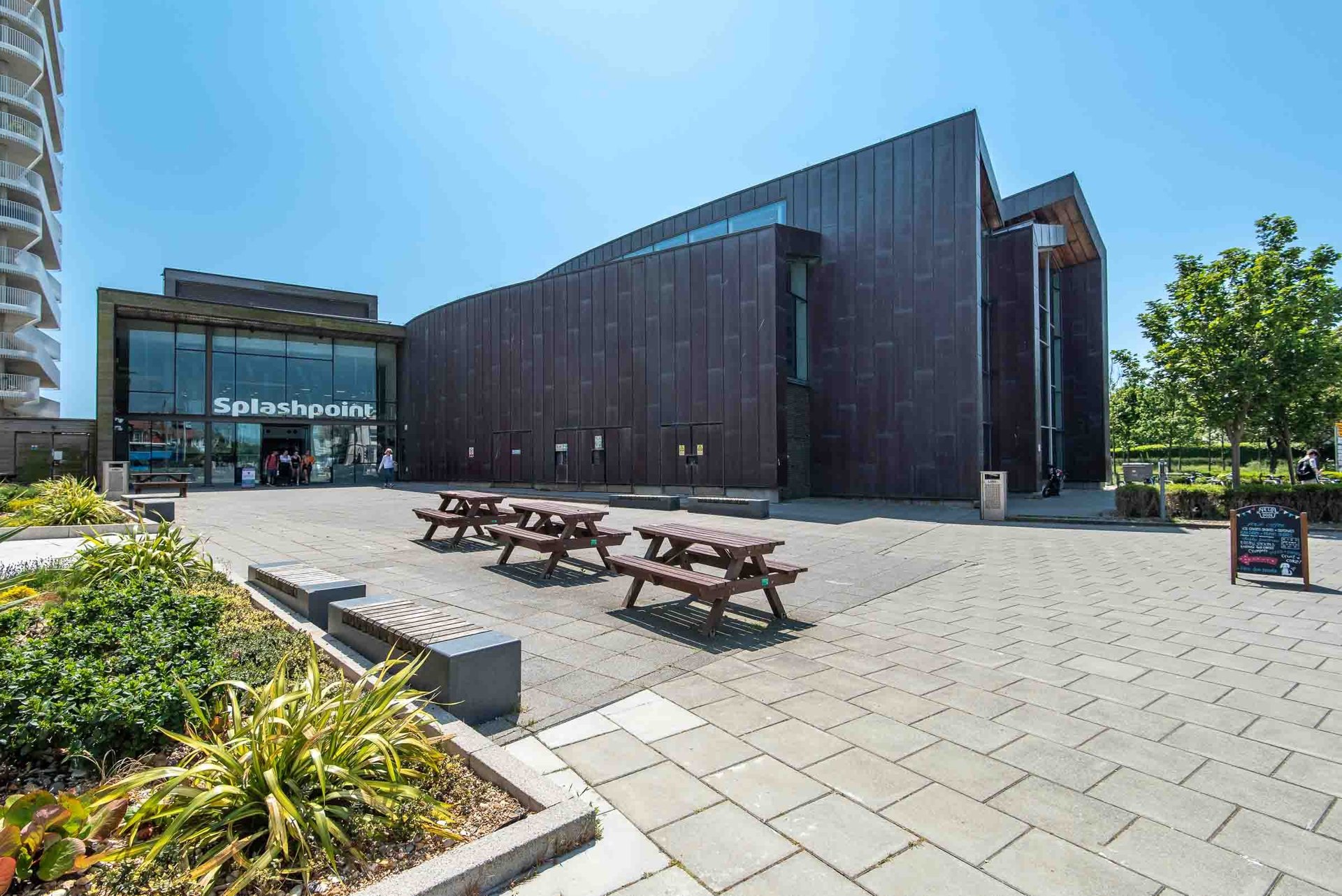 The dark timber-clad Splashpoint leisure centre and its sunny plaza with picnic tables