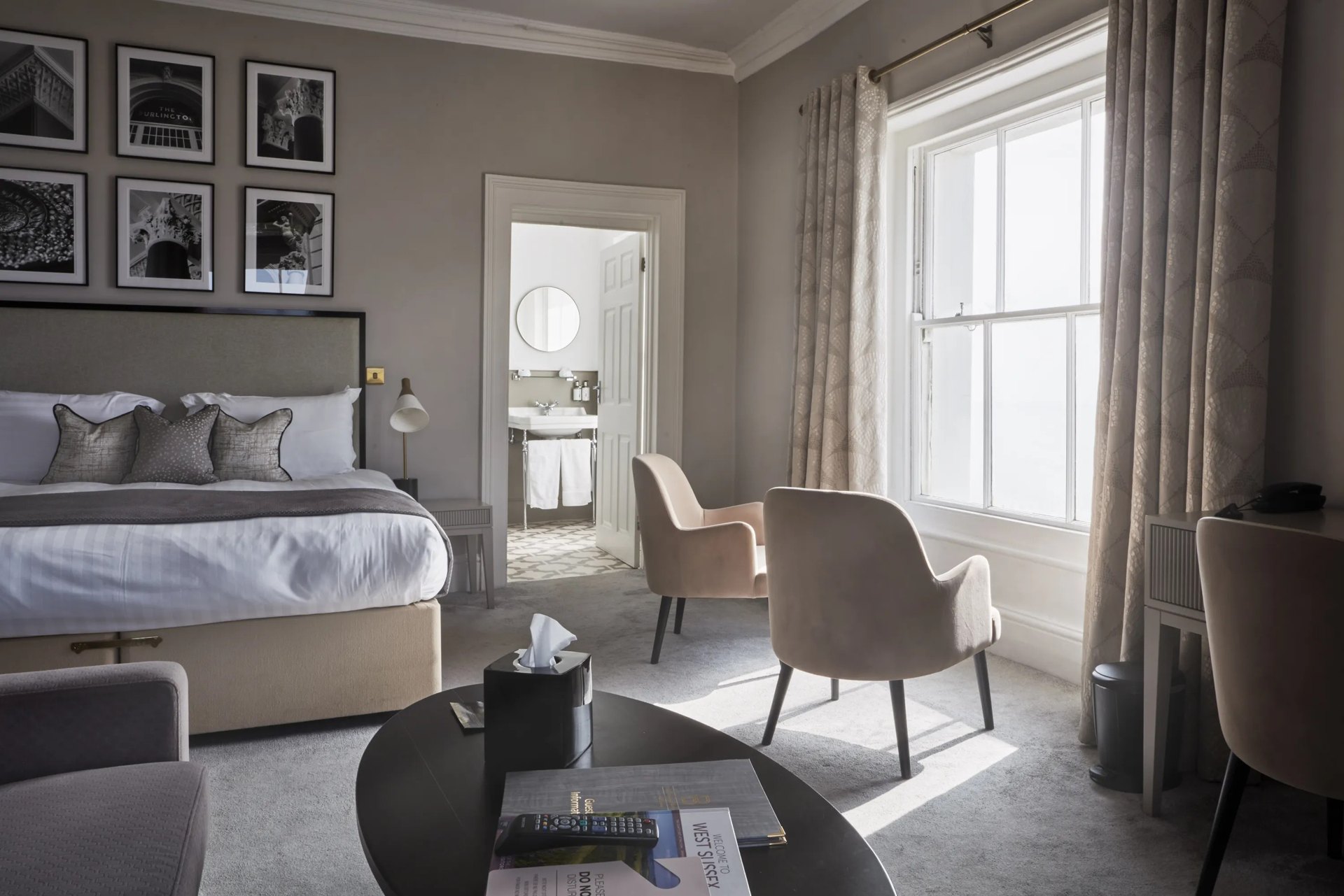 A bedroom at The Burlington, with grey upholstered chairs, framed photographs and a tall sash window