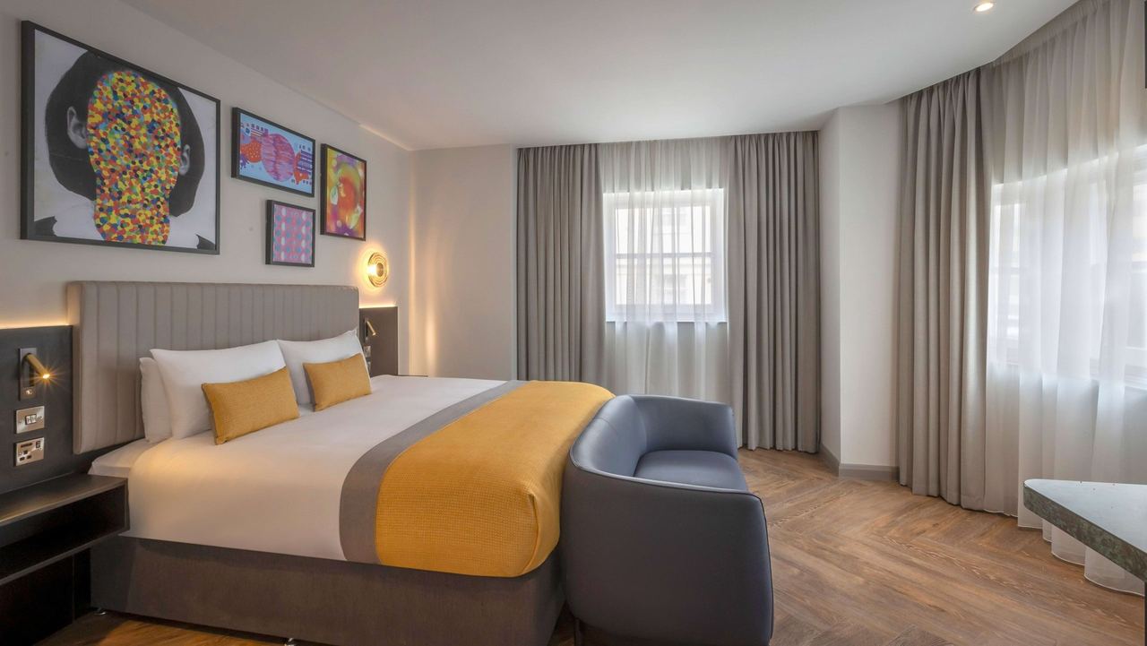 A bedroom at the Maldron Hotel Brighton with a yellow throw and bright pop-art prints