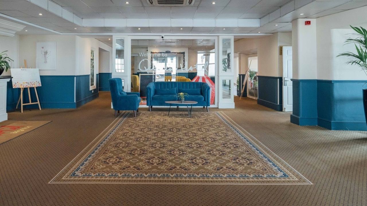The lobby of the Queens Hotel, with blue armchairs and a patterned rug