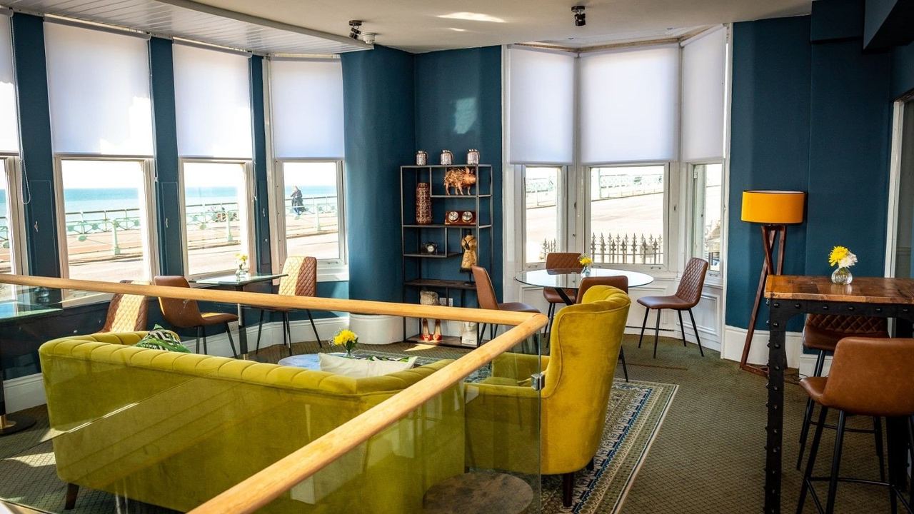 A lounge at the Queens Hotel with green sofas and tall windows over the seafront