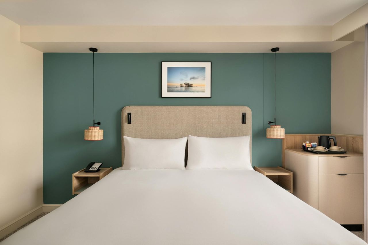 A refurbished bedroom at the Old Ship Hotel with a teal wall and a seaside print