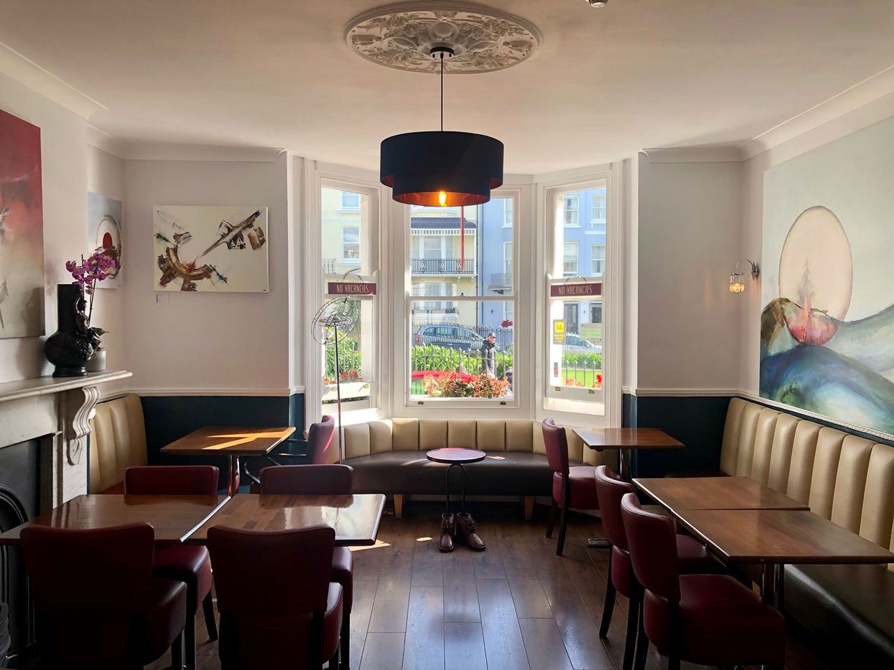 The breakfast room of the New Steine Hotel, with a bay window, banquettes and a ceiling rose