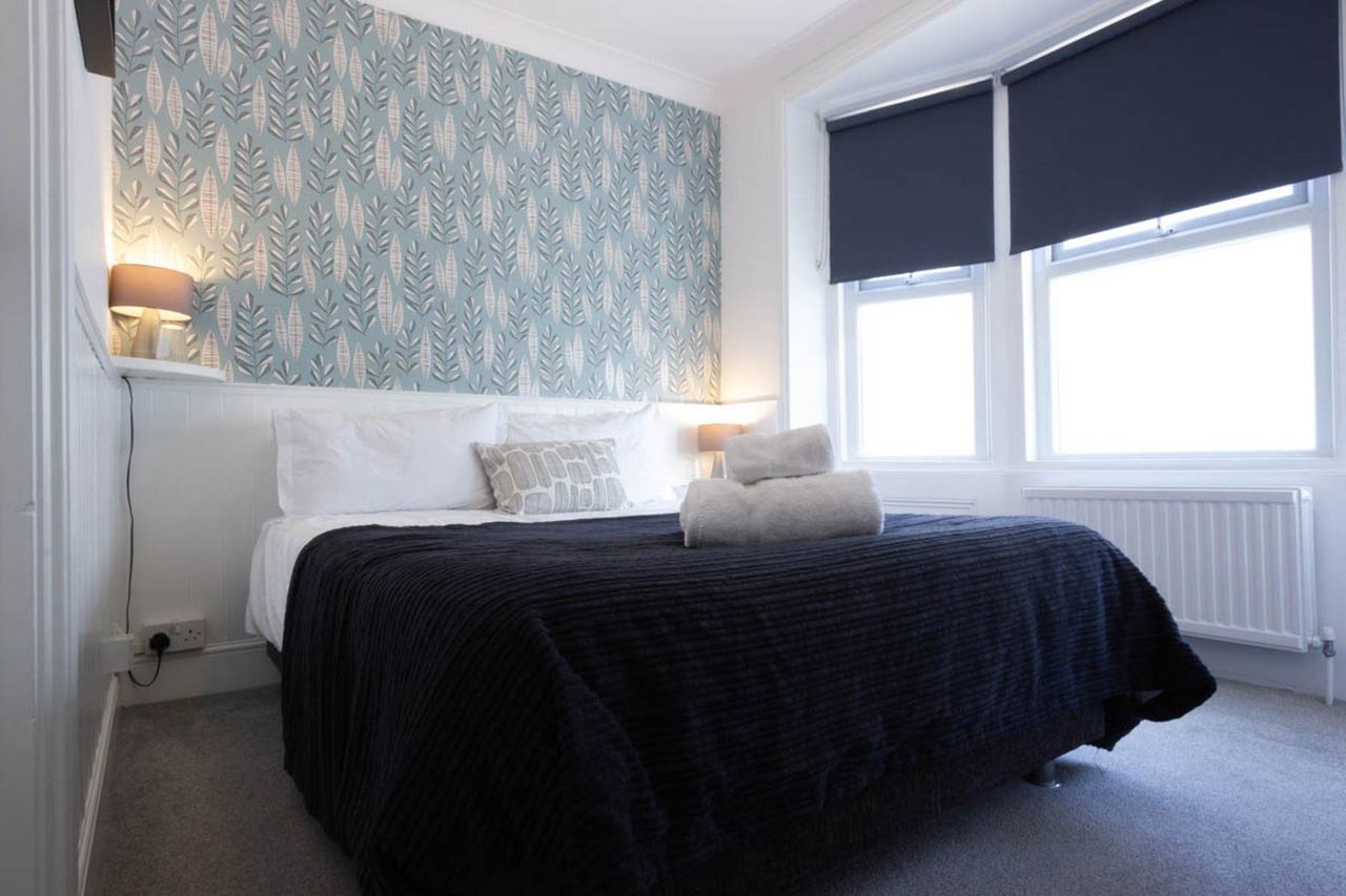 A bedroom at The White House with leaf-print wallpaper and a navy bedspread
