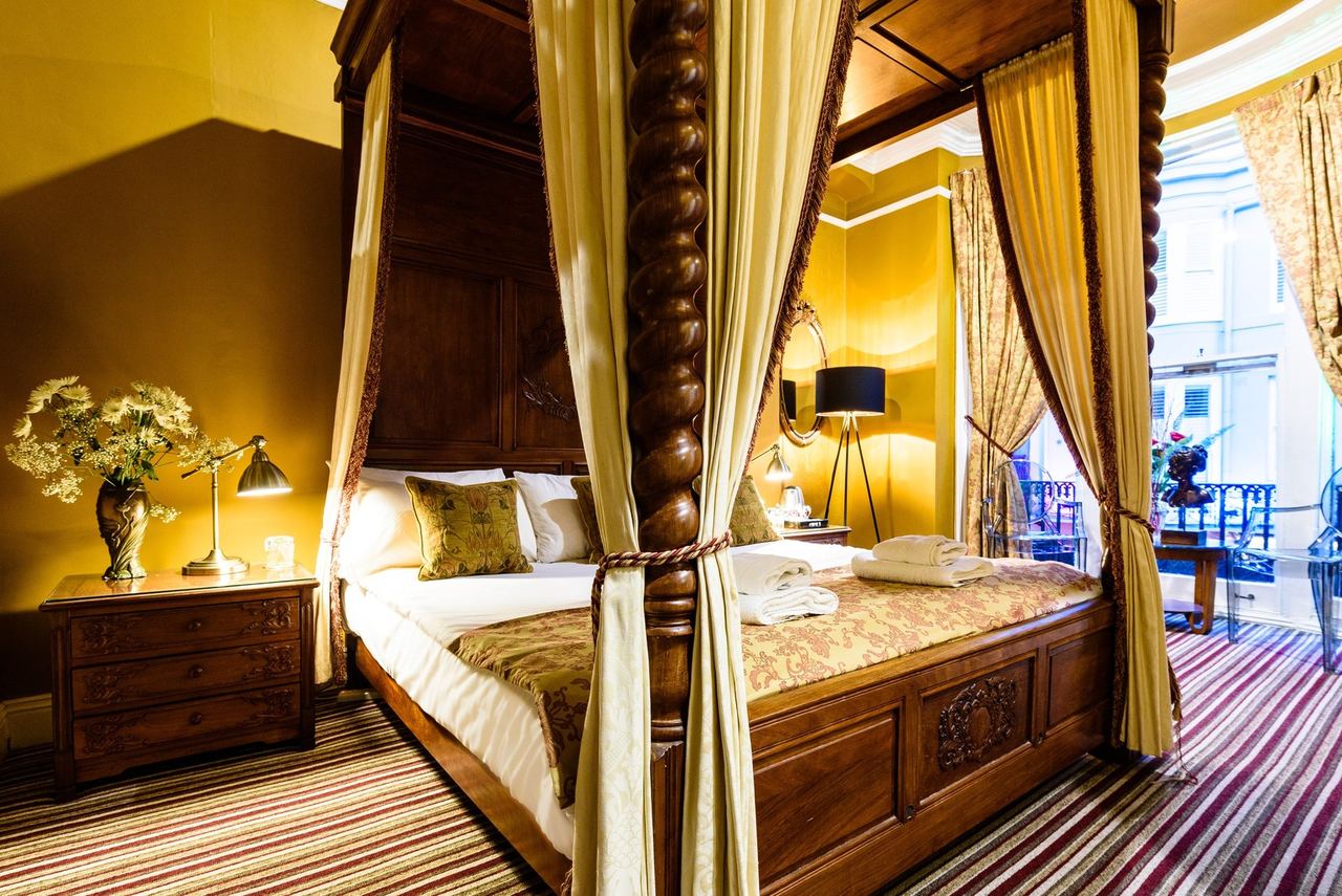 A four-poster room at Paskins Town House with gold curtains and striped carpet