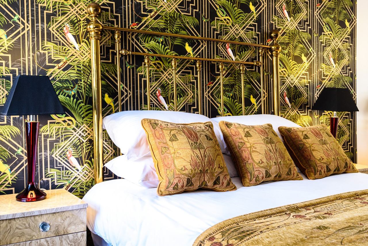 An Art Deco bedroom at Paskins Town House with gold palm wallpaper and a brass bed