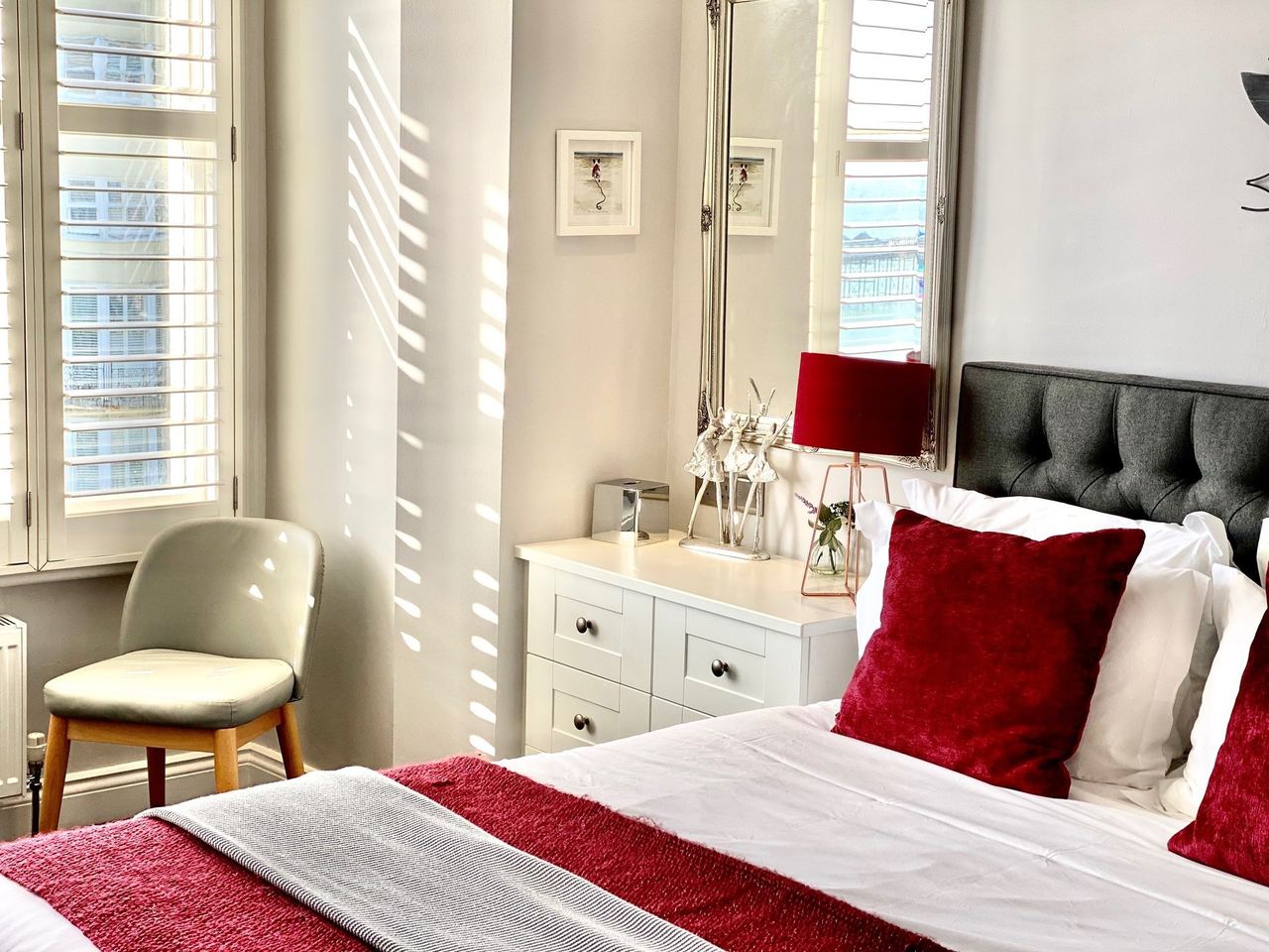 A bedroom at A Room With A View with shutters, red cushions and a sea view