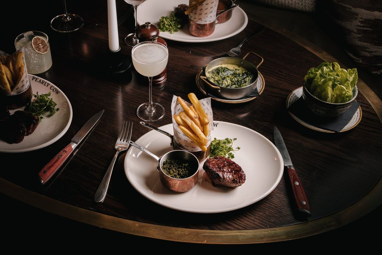 Steak, fries and sauces on a dark round table at Pearly Cow