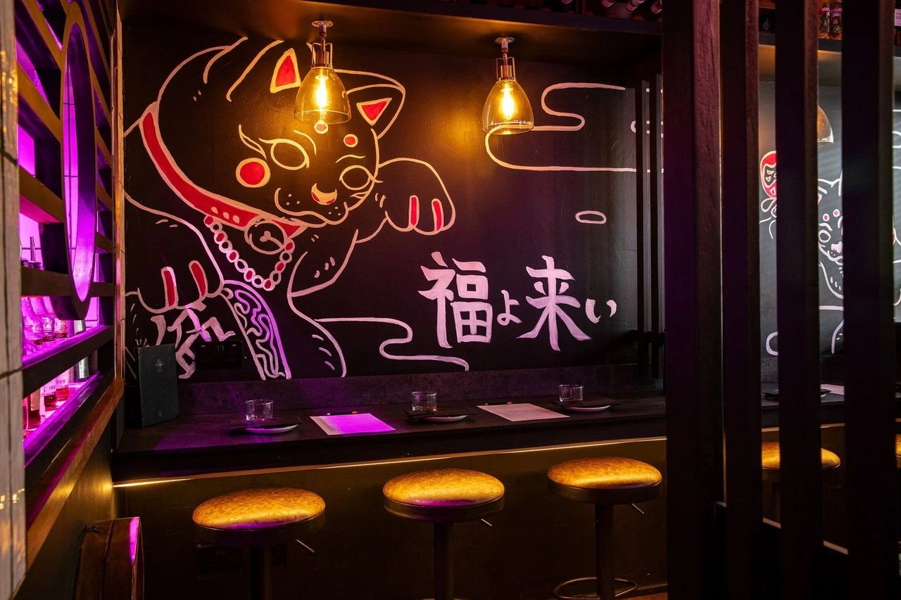 A dark corner of Bonsai Plant Kitchen with a lucky-cat mural and bar stools