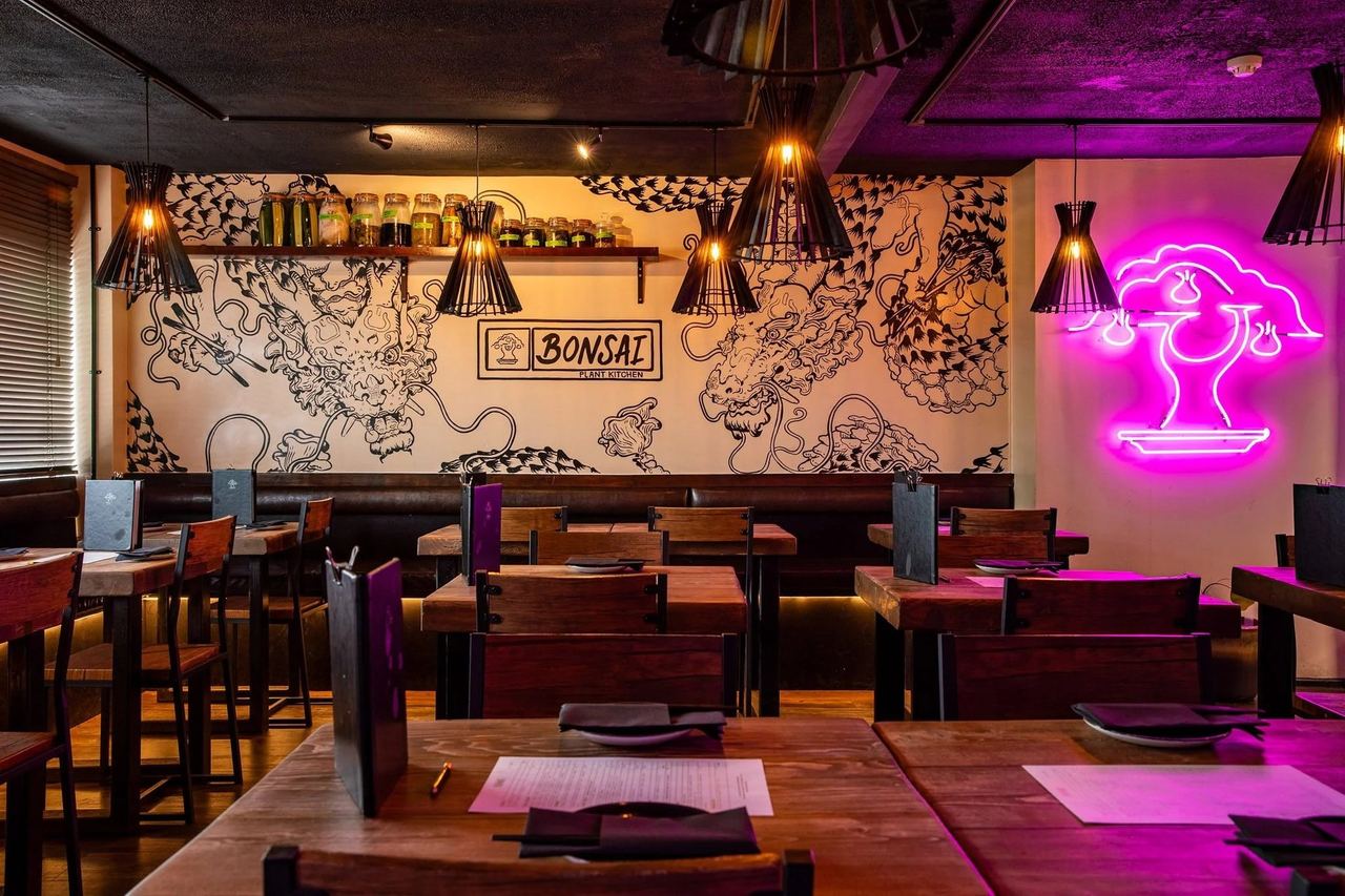 The dining room of Bonsai Plant Kitchen, with an ink-drawn mural and a pink neon bonsai