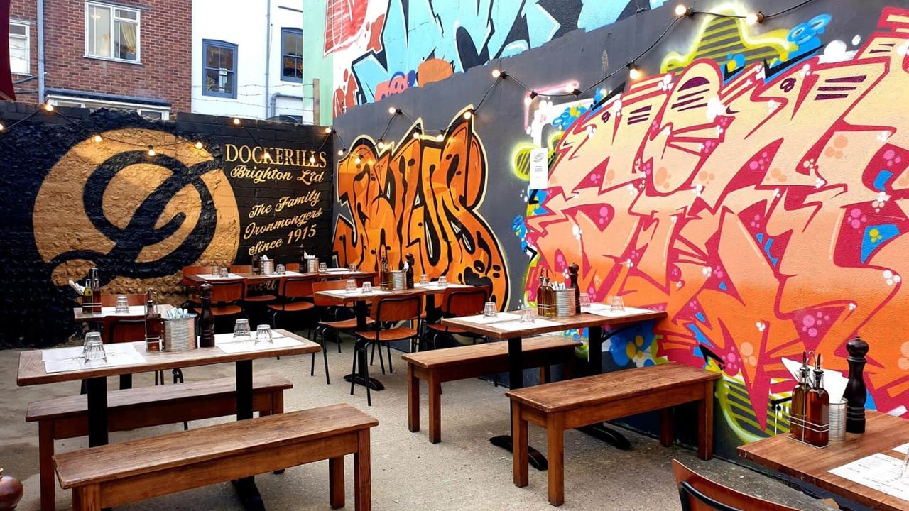 The courtyard of Franco Manca Brighton, with long benches and graffiti murals