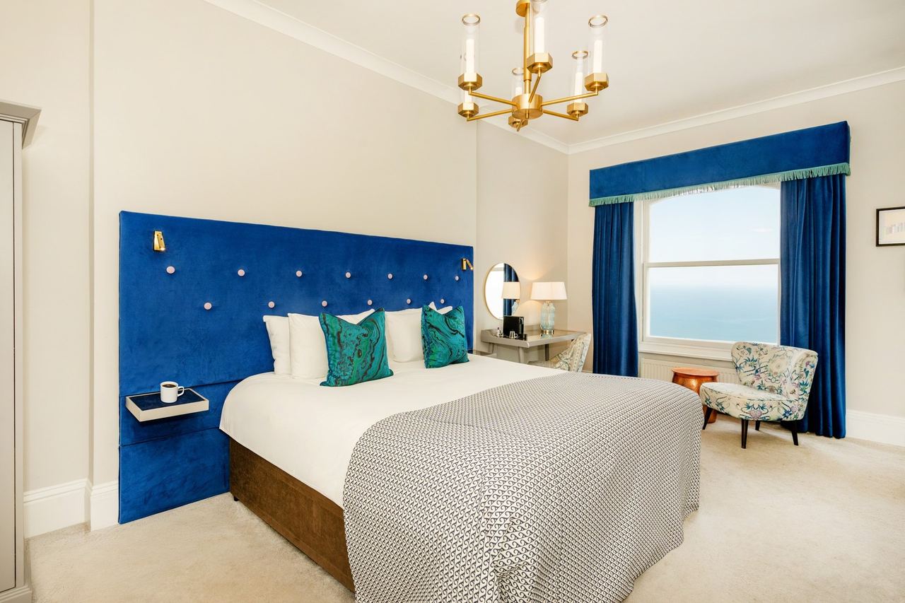 A sea-view bedroom at the Mercure with a blue velvet headboard and a chandelier