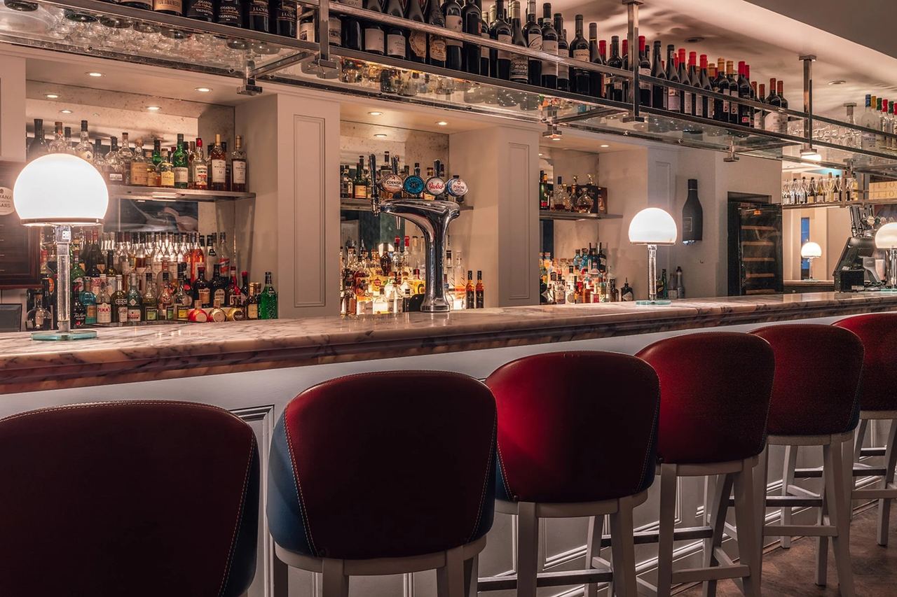 The bar at HarBar + Kitchen, with red stools and shelves of bottles