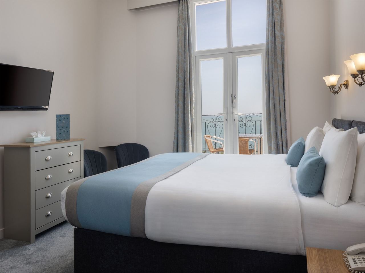 A bedroom at Hotel Cumberland with French windows to a balcony over the sea