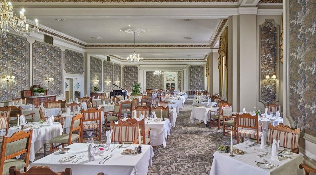 The Garden Room at The Grand, with chandeliers, patterned walls and tables in white linen