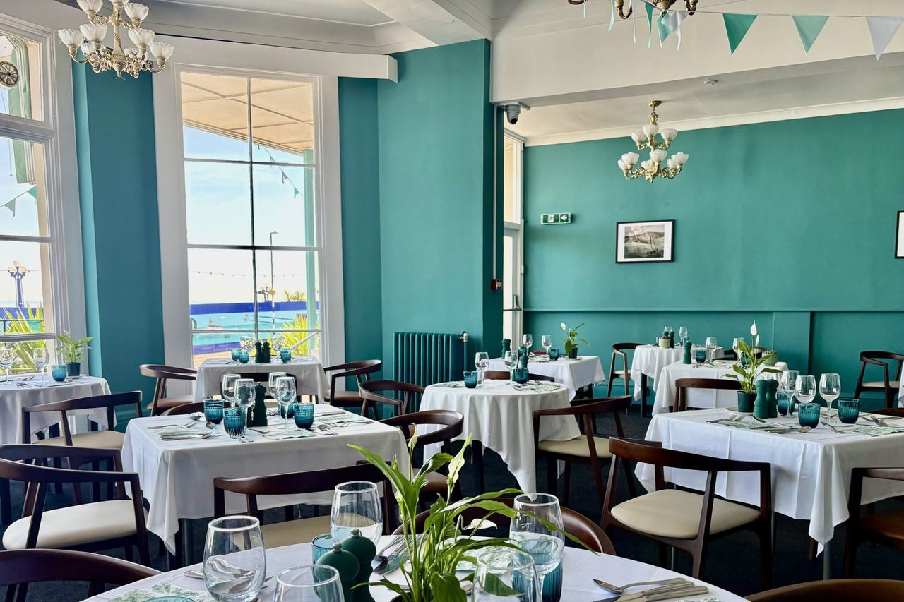 The sea-view restaurant at Hotel Cumberland, teal walls, chandeliers and tables laid in white