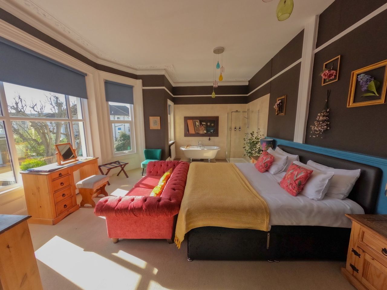 A bay-windowed bedroom at The Sheldon with a red velvet sofa and a roll-top bath
