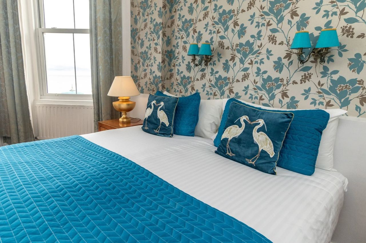 A bedroom at Hotel Cumberland with heron cushions and leaf-print wallpaper