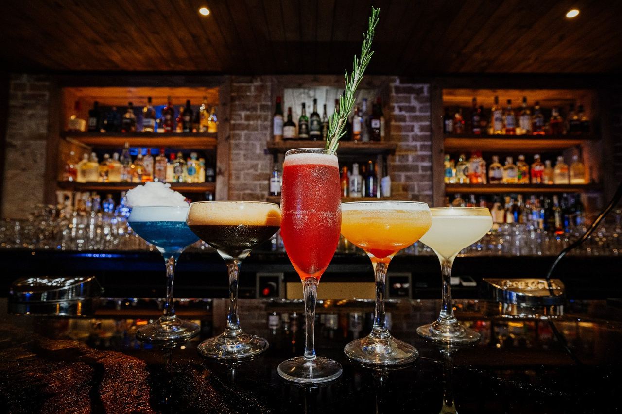 Five cocktails on the bar at Eastbourne Cocktail Club, shelves of bottles behind