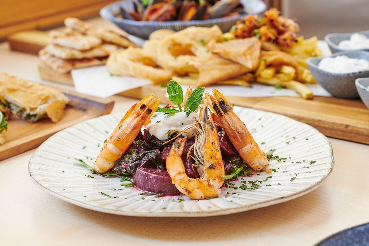 Grilled prawns on beetroot with meze and filo pies behind at gr/eat Greek Cuisine