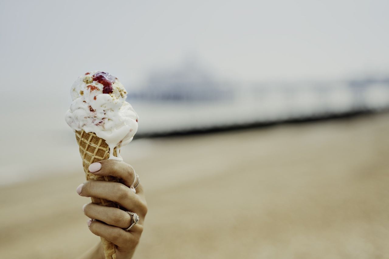 A cone of gelato held up on the beach, the pier blurred behind, from Gelato Famoso